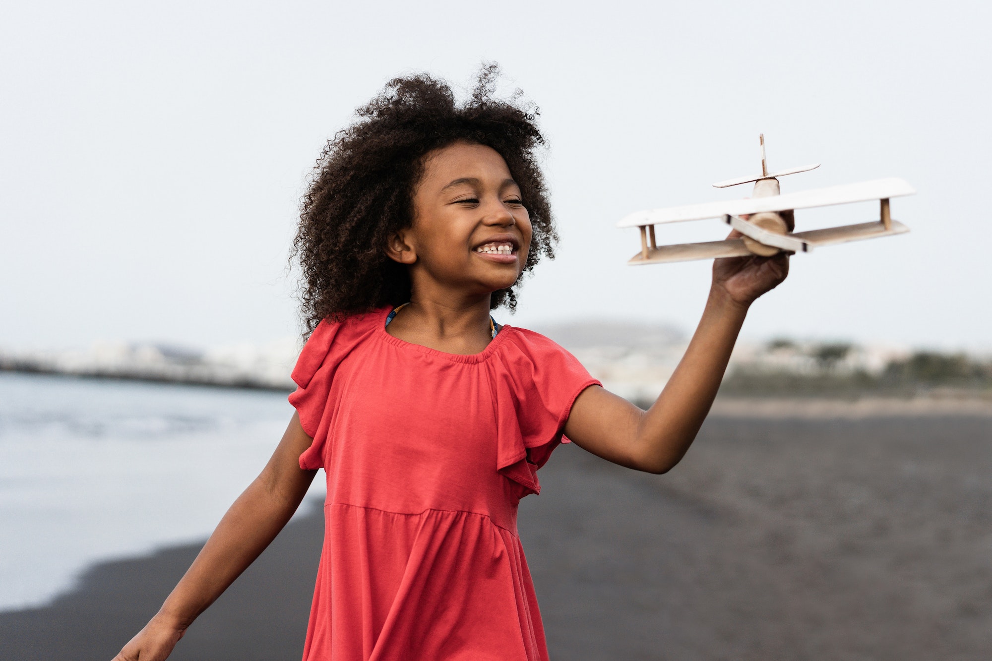 African kid running on the beach while playing with wood toy airplane - Focus on face